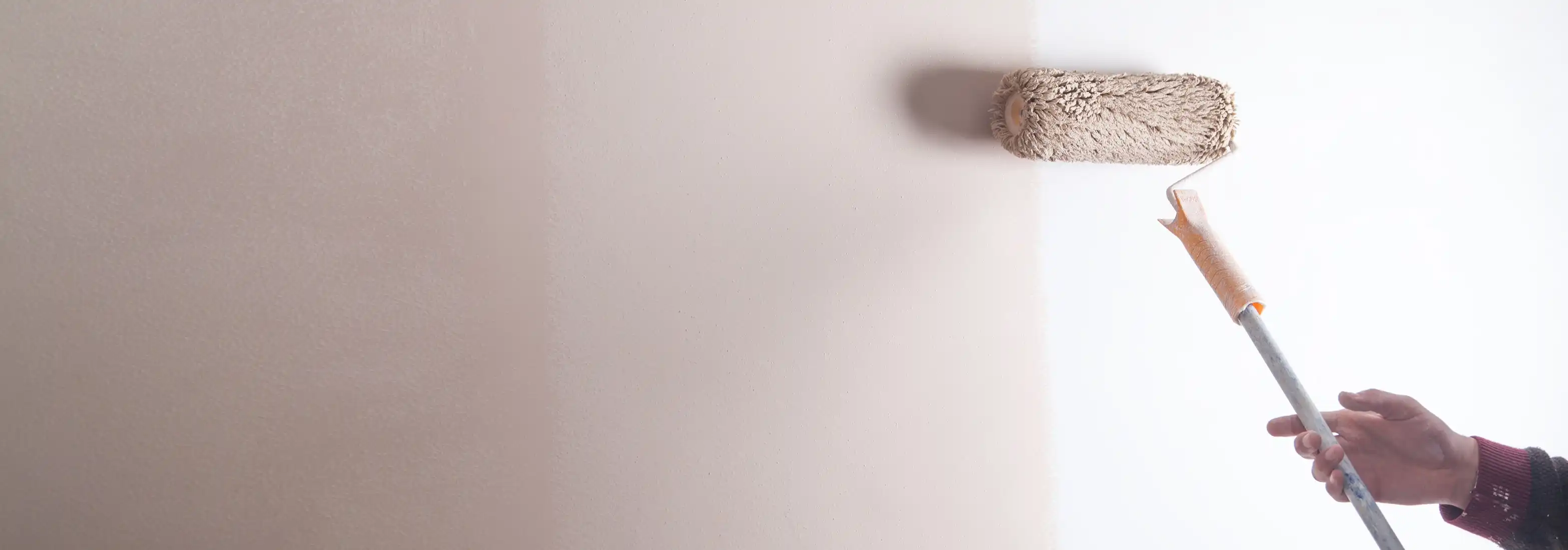 Rouleau appliquant une peinture rosée sur un mur blanc
